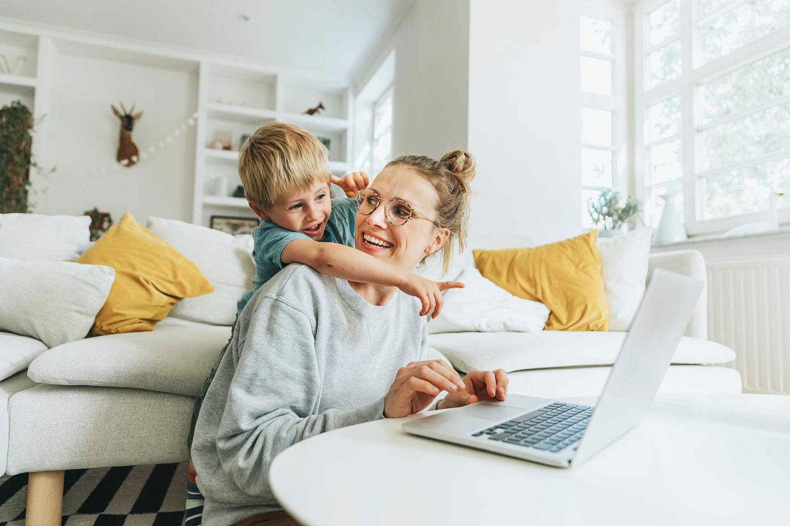 Eine Frau sitzt am Laptop, ihr Sohn umarmt sie und zeigt auf den Bildschirm